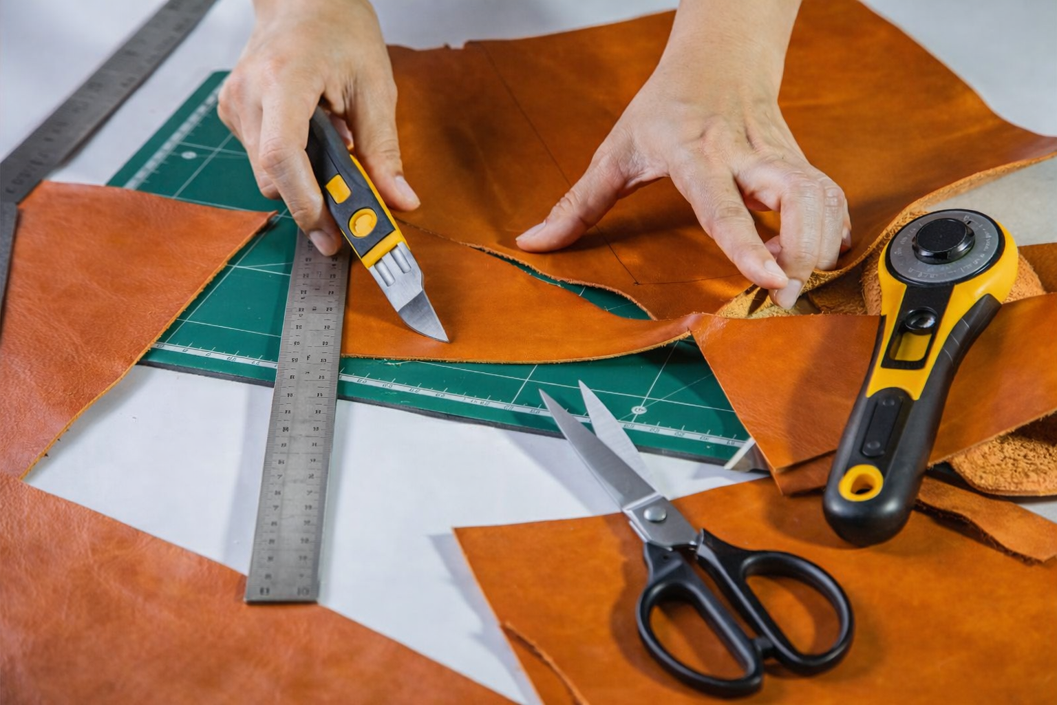 cutting leather with a utility knife and metal ruler on a cutting mat