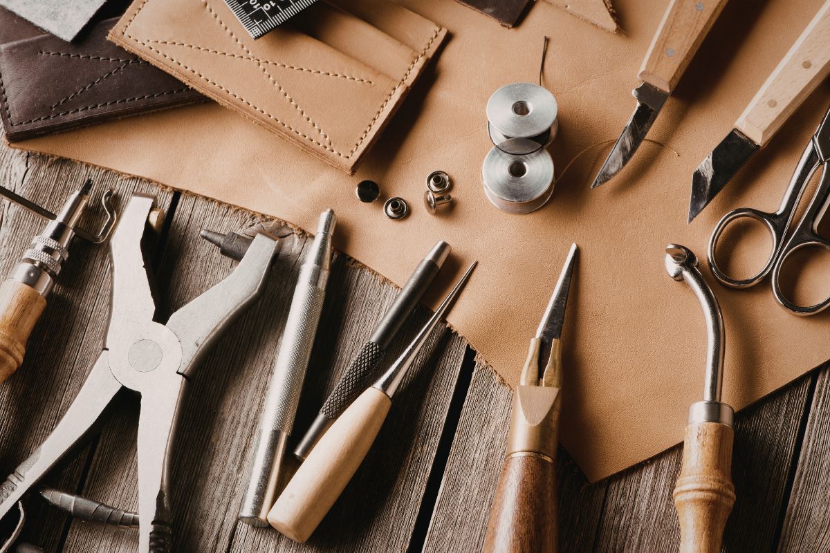Essential leathercraft tools for beginners including awl, knives, thread, scissors and leather pieces